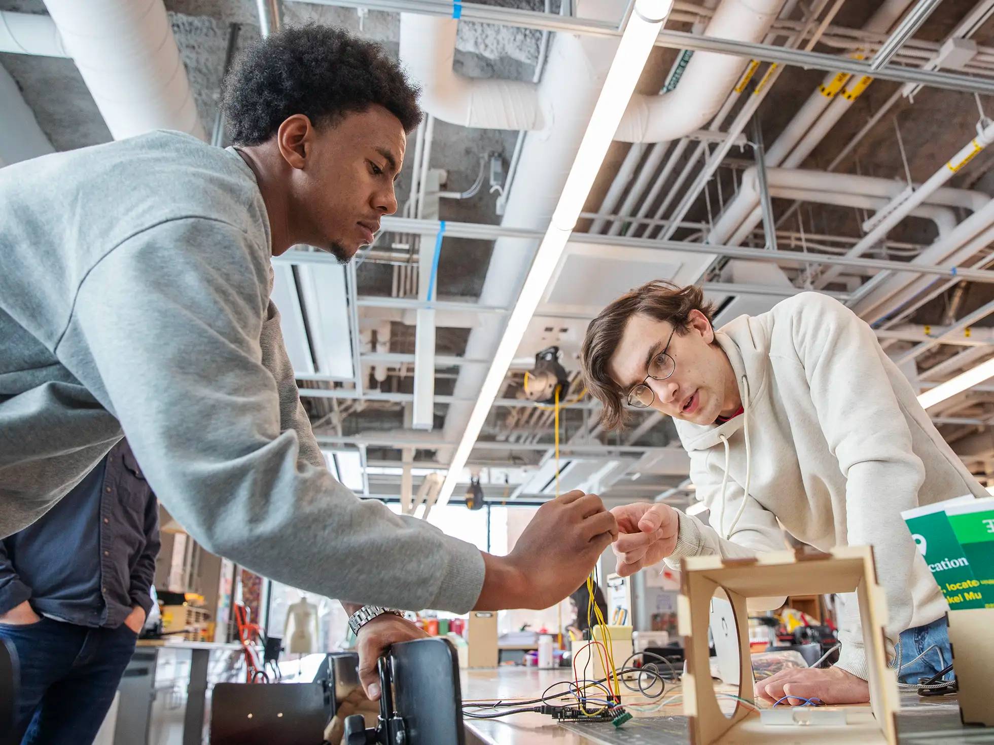 Two Skidmore College students collaborate on an electronics project in the IdeaLab, carefully connecting wires to a circuit board in a bright, modern makerspace.