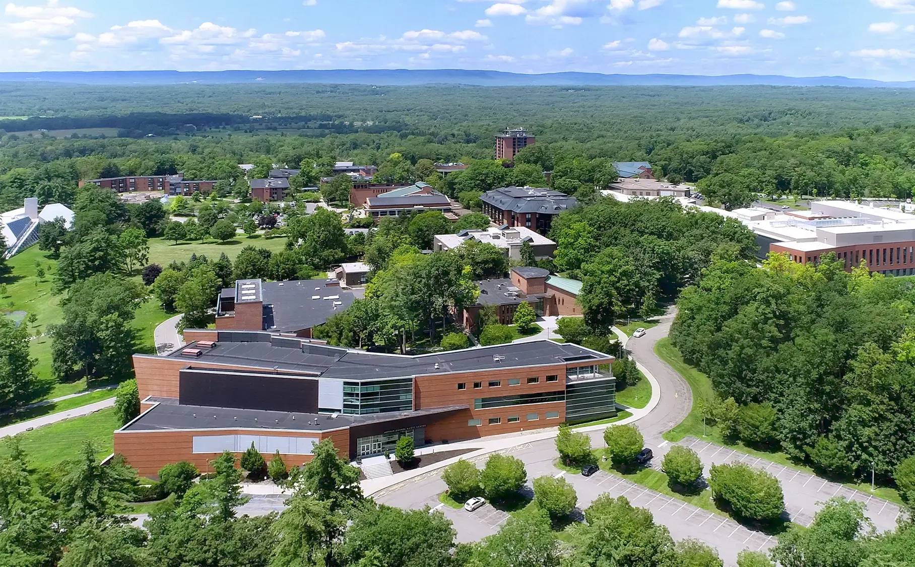Aerial view of Skidmore College’s campus on a sunny day, showcasing academic buildings, residence halls, and green spaces surrounded by lush trees.