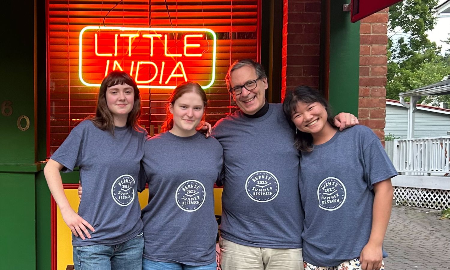 Professor Bernard Possidente and his students, including Jordan Diamond ’27, outside Little India in Saratoga Springs wearing matching 2025 summer research shirts.