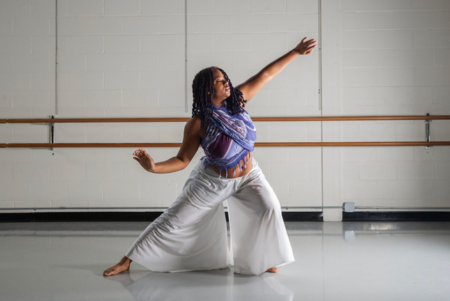 Aminah Hopewell with her arms diagonally outstretched as she dances in a Skidmore studio