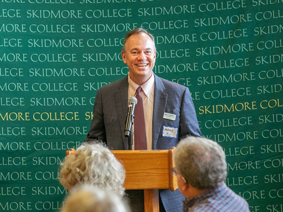 President Marc C. Conner presenting to an audience at a podium with a Skidmore banner in the background