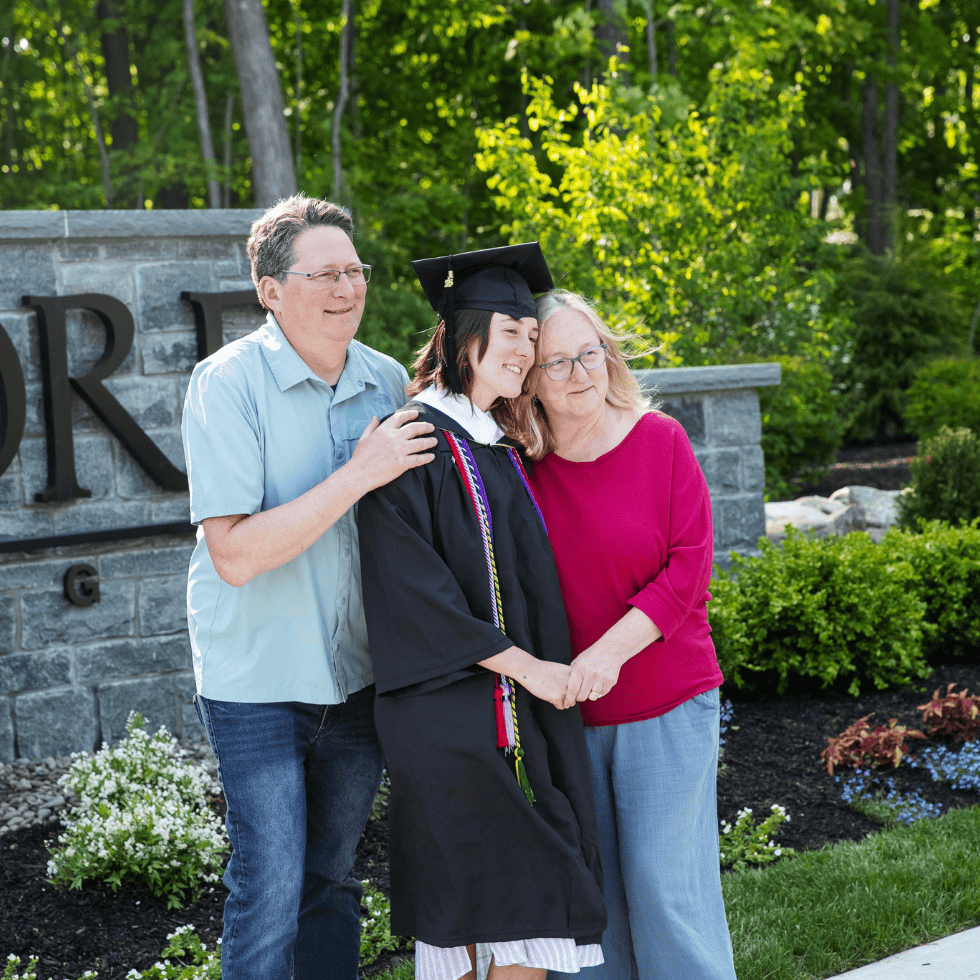 Parents embrace their student, who is wearing their graduation gown, outside Skidmore's main entrance.