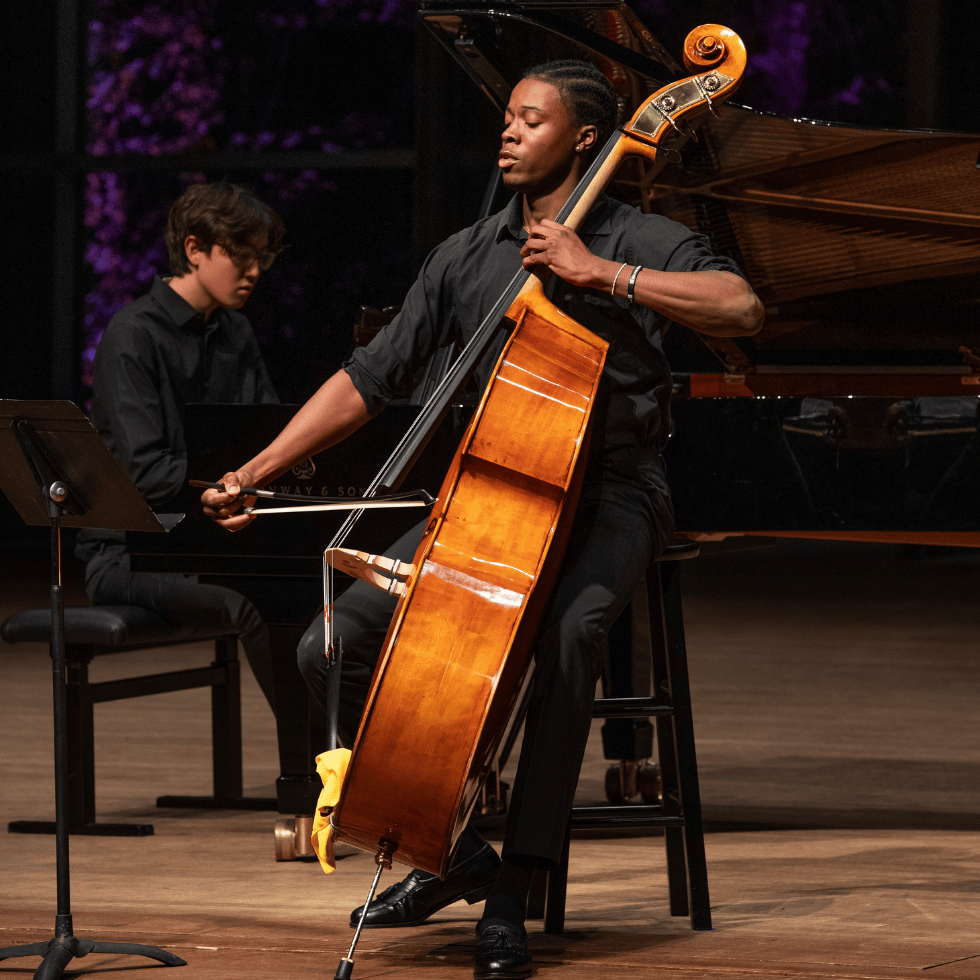 Cellist plays on stage along with piano player in background
