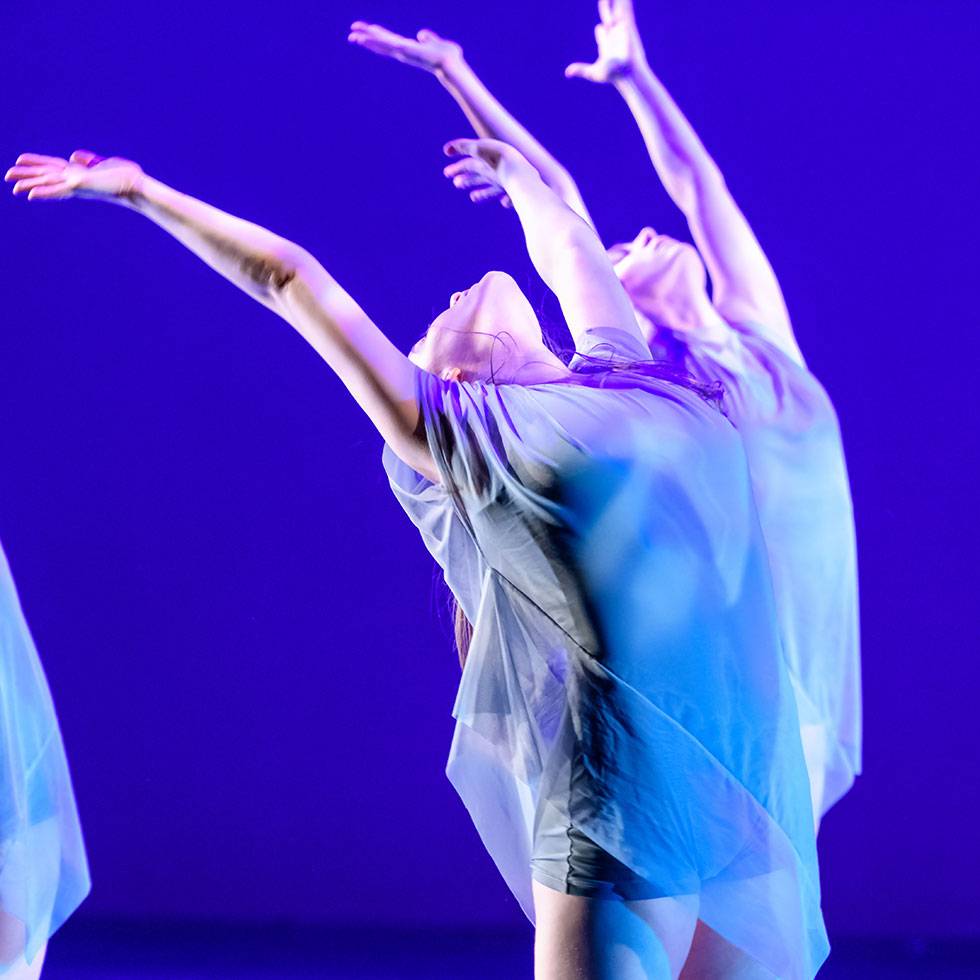 Student dancer performs on stage with head thrown back and arms raised into the air