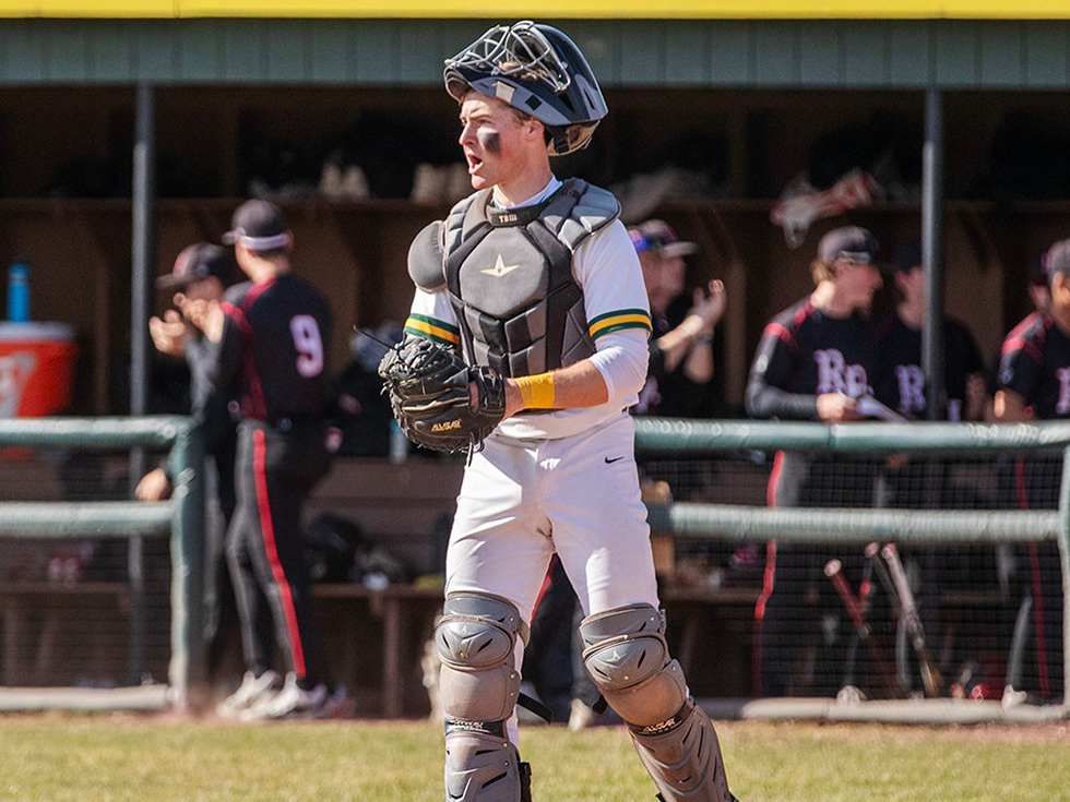 Trey Borque in baseball catcher gear stands on a field.