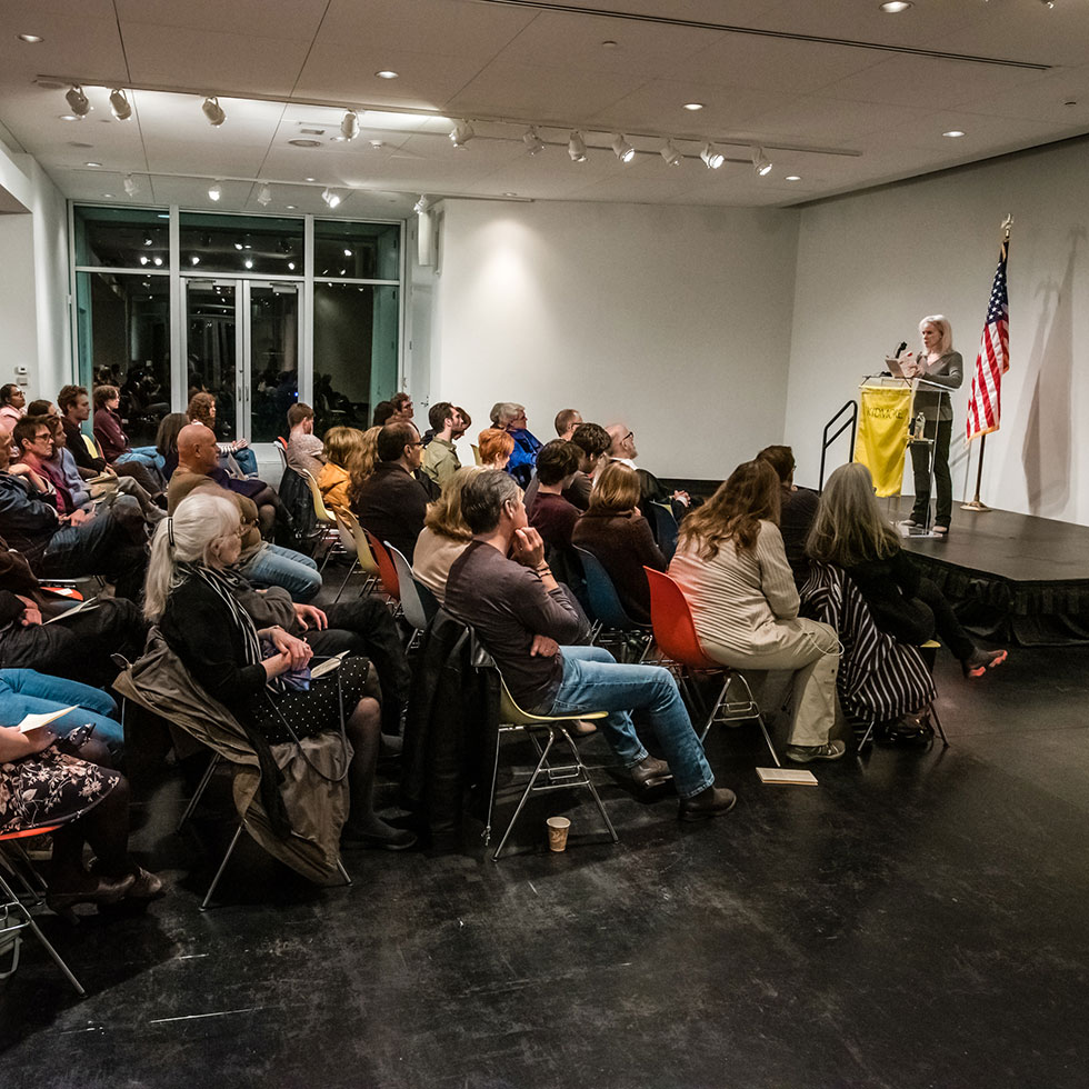 An audience sits listening to a speaker on stage in the Tang Museum's Payne room