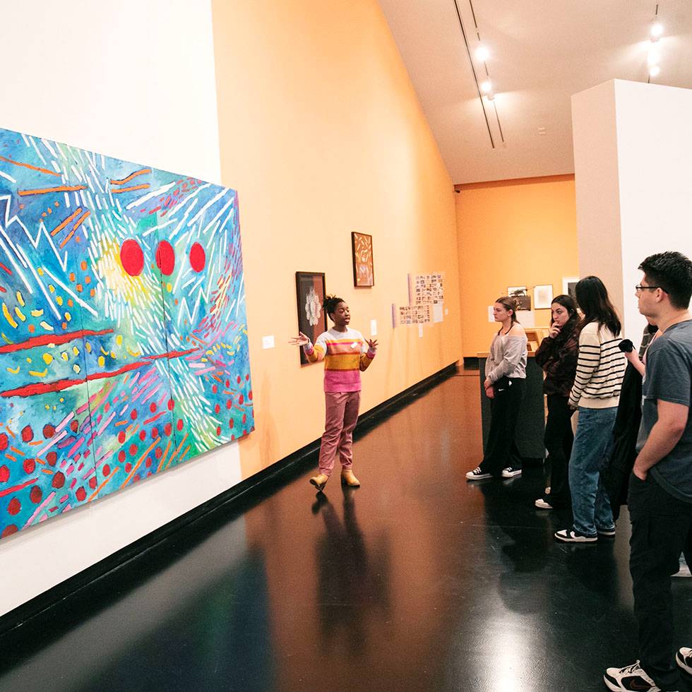 Student shows a group a piece of art work while giving a tour of the Tang Teaching Museum