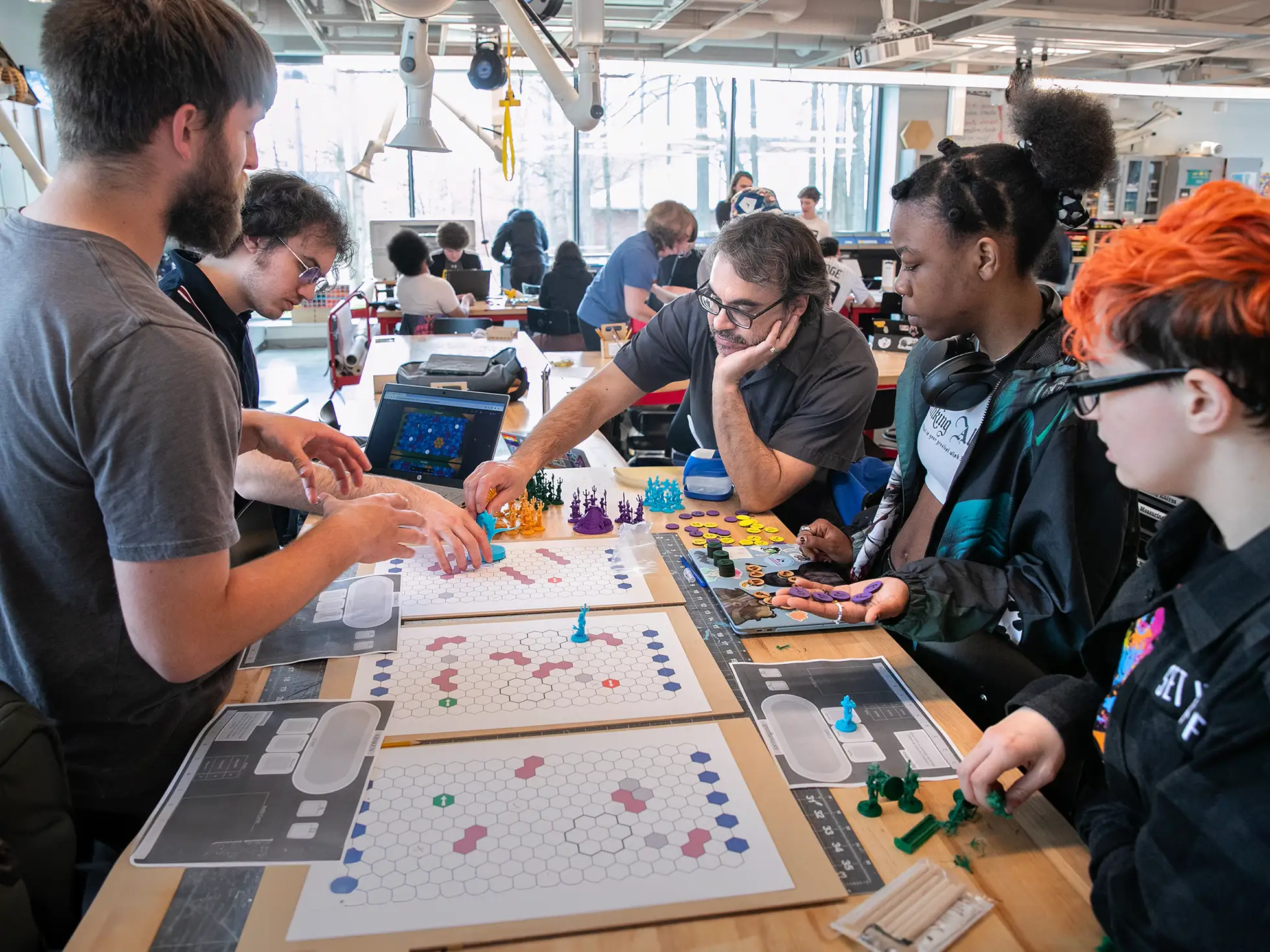 Students in Skidmore College’s Tabletop Game Design class collaborate around a game board covered with custom pieces and hexagonal maps in the IdeaLab makerspace.