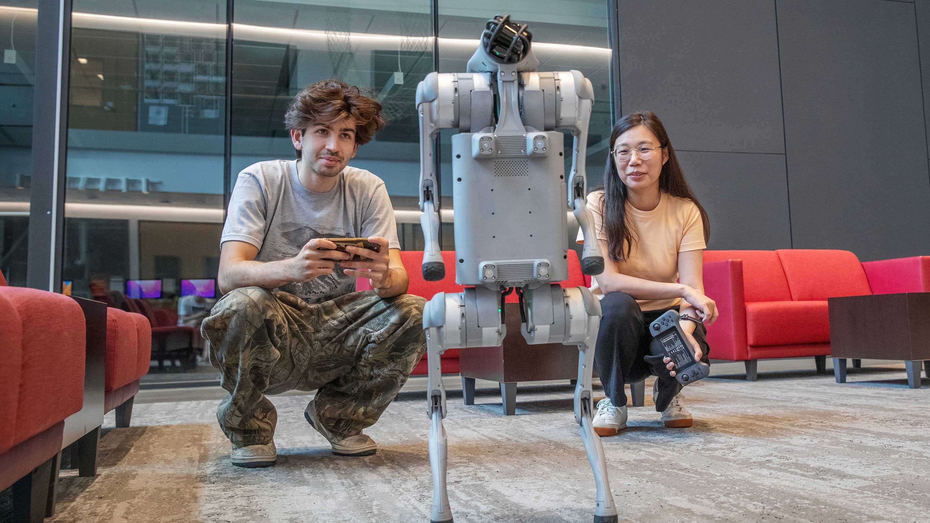 A Skidmore faculty member and a student use handheld controllers to operate a four-legged robot in Skidmore's Billie Tisch Center for Integrated Science lobby.