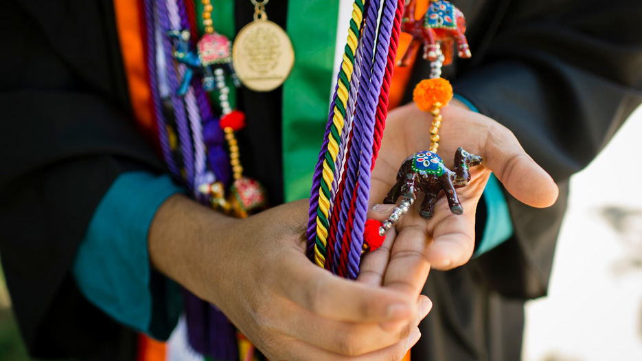 College graduate holds various colored regalia and cords in their hands