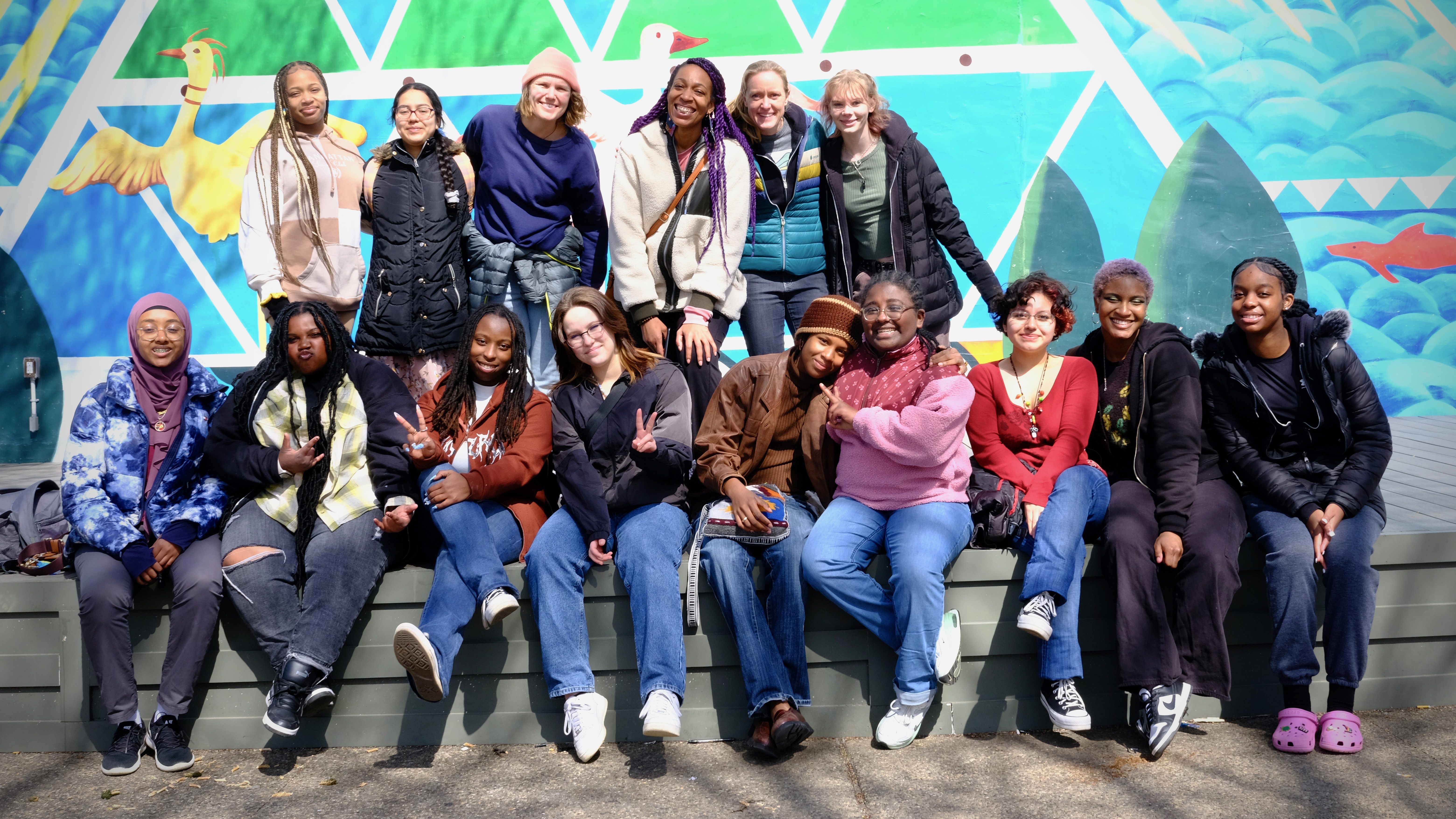 A group of students in a Field Academy East Coast tour pose against a mural with Anna Graves ’14 and Danika Robison ’10. 