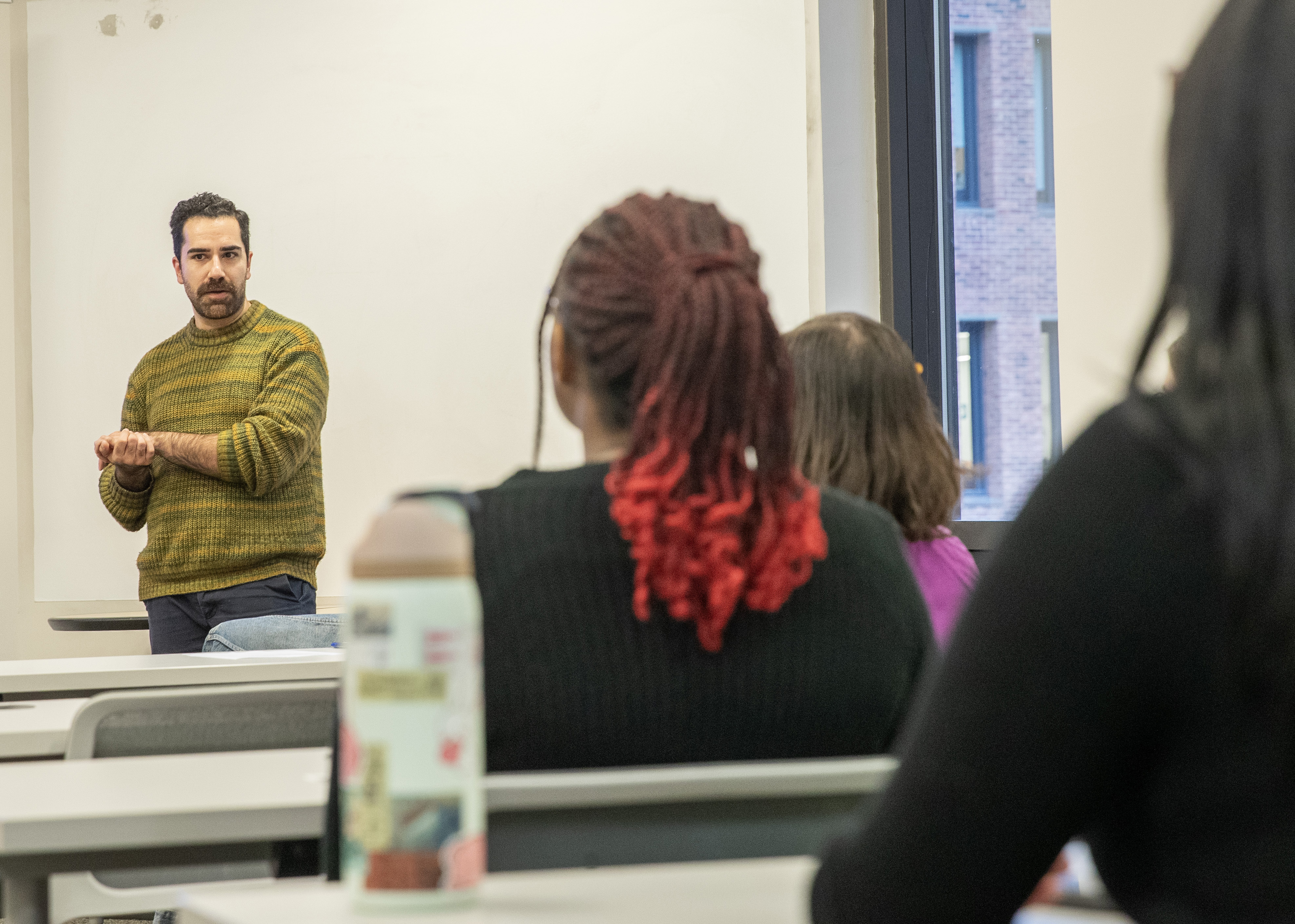 Jamie Parra stands at the head of the LEDS classroom in front of several rows of students.
