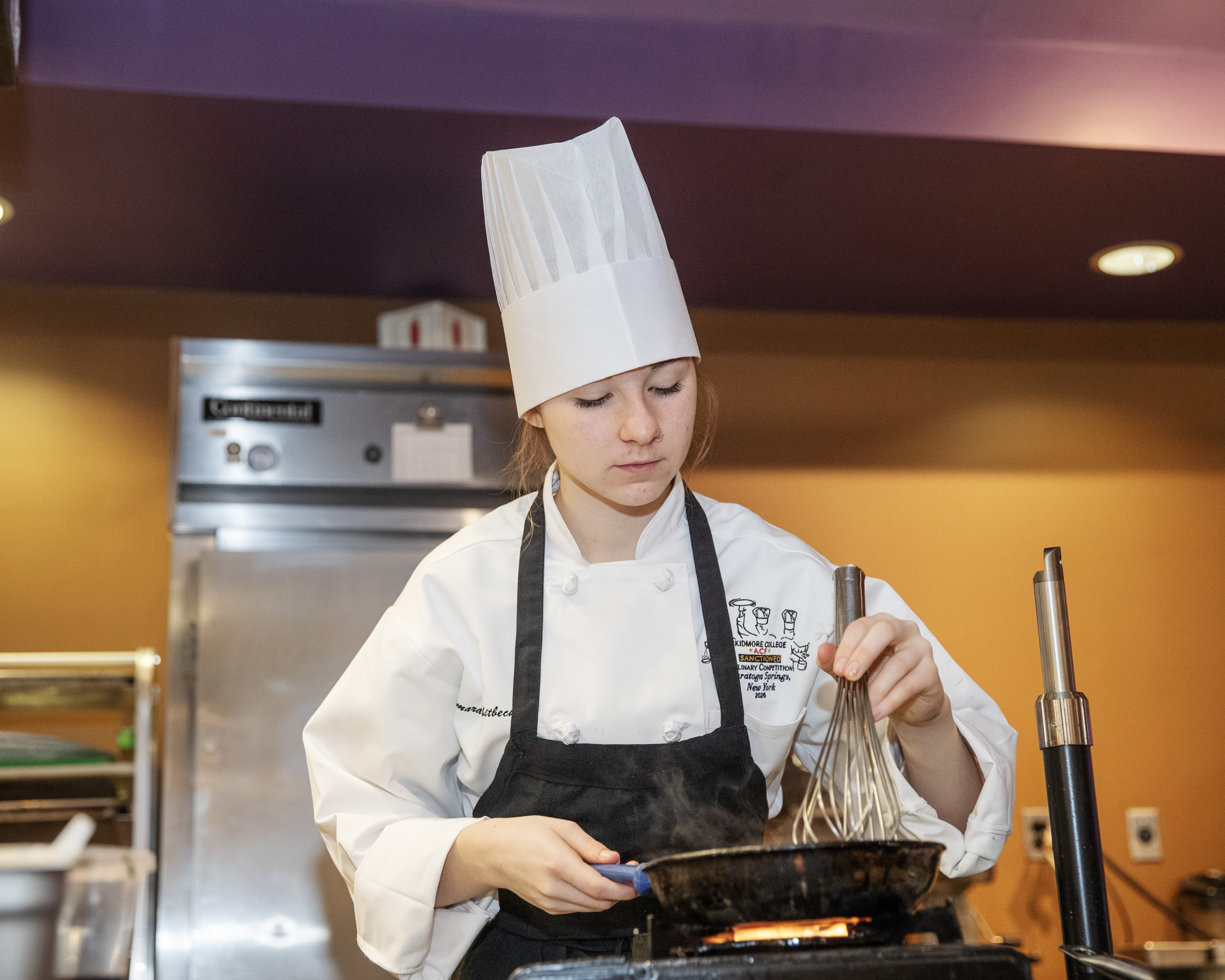 Sommarah Whitbeck uses a metal whisk in a small pan over a flame
