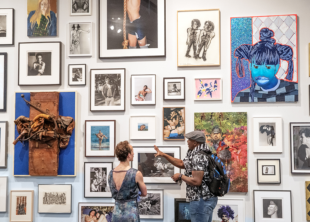 To people stand in front of a gallery wall in the Malloy Wing, engaged in conversation.