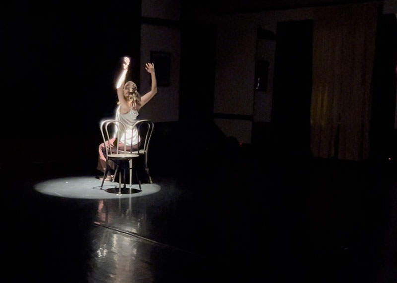 Gunter crouches, stretching a long piece of rope above her head on a blue-lit stage.