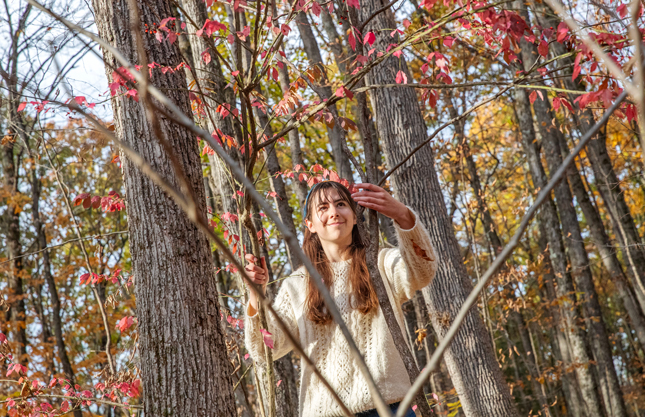 A student looks at leaves in Skidmore's North Woods