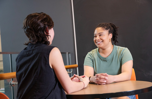 Two students talk while siting at a table