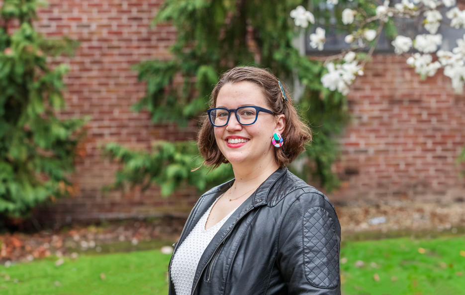 Sarah Faude stands outside on the Skidmore campus, in front of a brick building and greenery