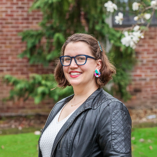 Sarah Faude stands outside on the Skidmore campus, in front of a brick building and greenery