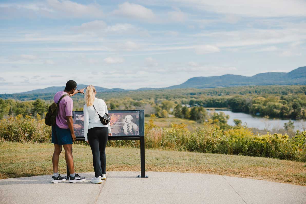 Two visitors look out over rolling hills and the Hudson River from a scenic overlook at Saratoga National Historical Park.