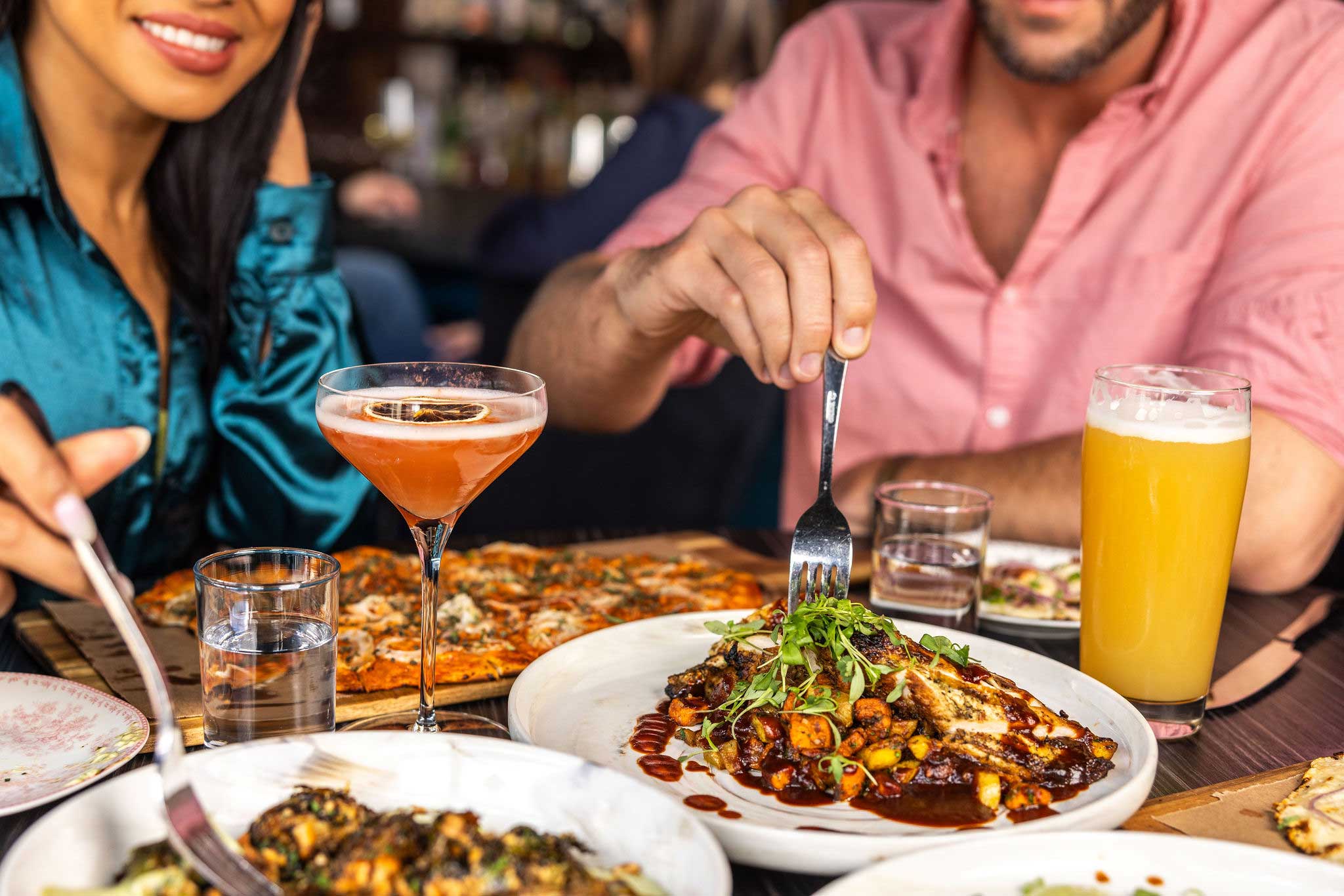 Diners share plates, pizza, cocktails, and beer at a restaurant table in Saratoga Springs.