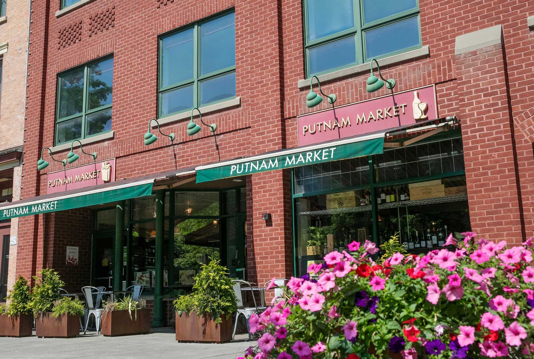 Putnam Market storefront in downtown Saratoga Springs with outdoor seating and bright pink flowers in the foreground.