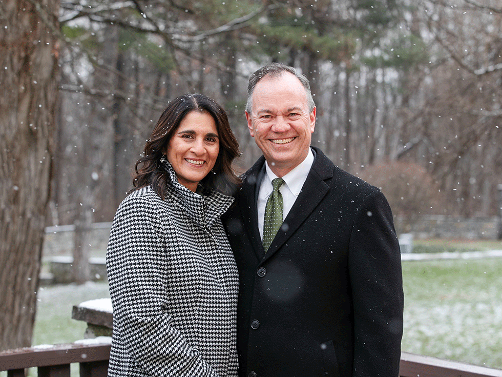 President Marc C. Conner and Barbara Reyes-Conner smile together while standing with their arms around the other, outside with a light snow falling.