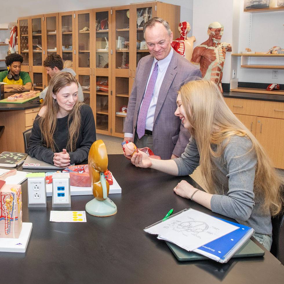 President Conner looks on over two students working in an anatomy and physiology lab.