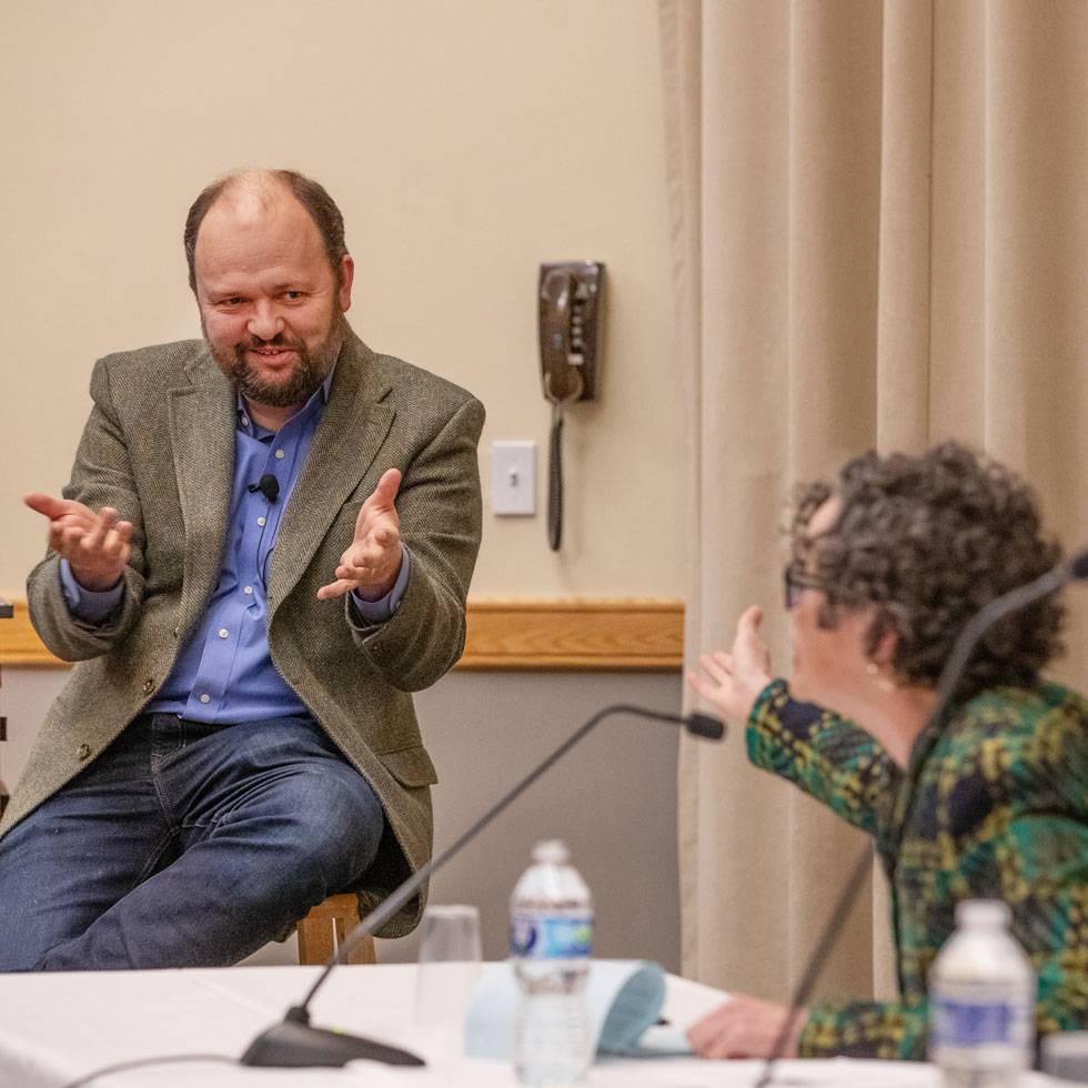 Ross Douthat smiles while talking to a Skidmore faculty member during a panel discussion.
