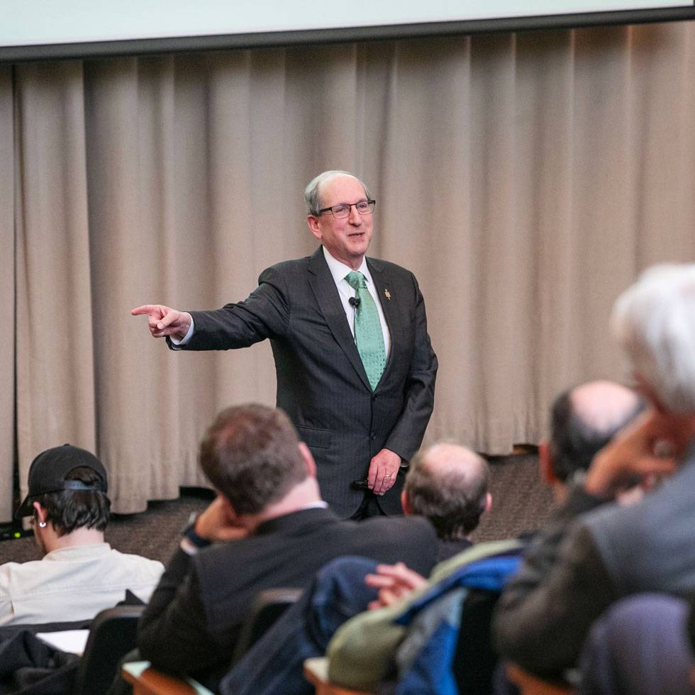 Frederick Lawrence stands at the front of an auditorium lecture hall while speaking to a group of students.