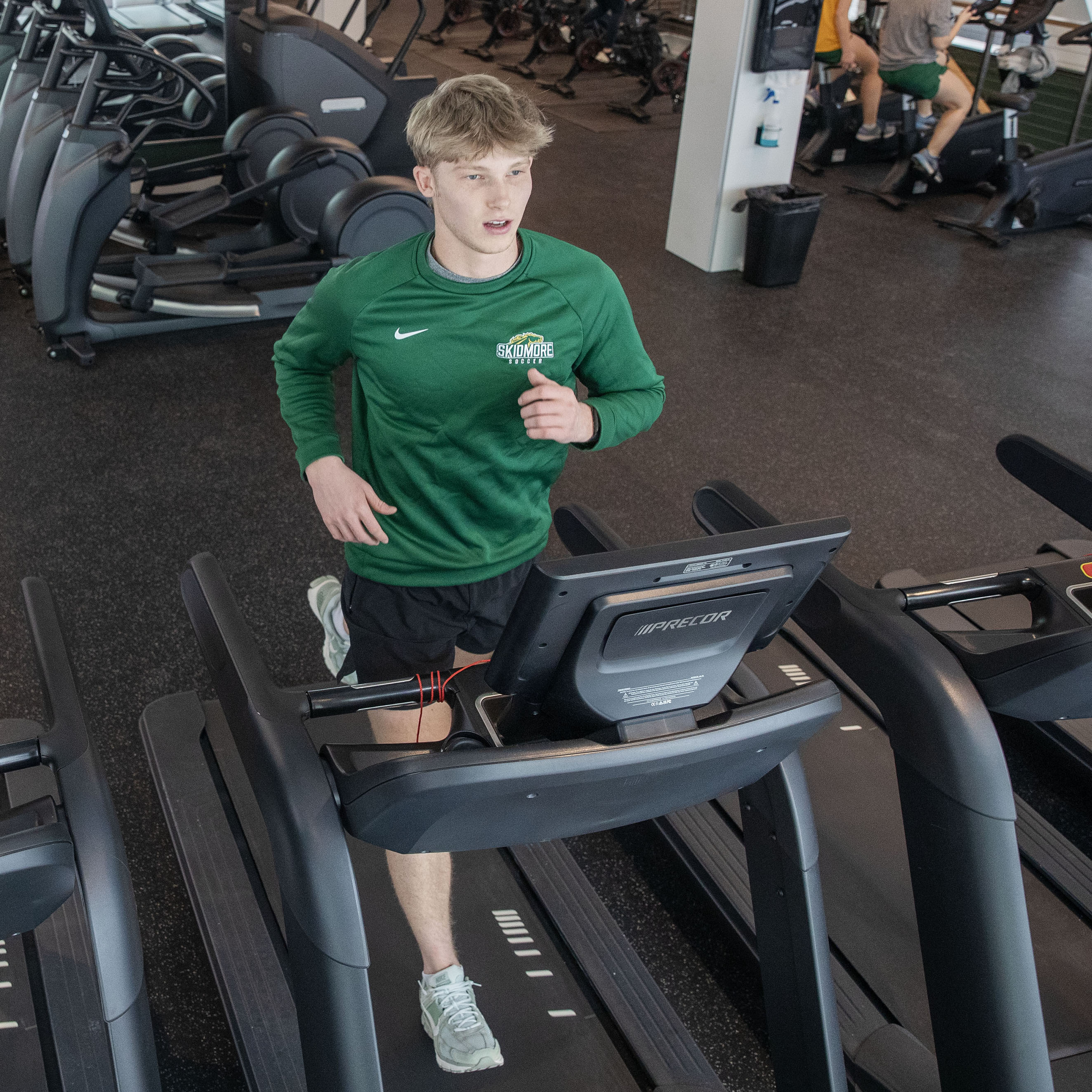 A student in a Skidmore athletic shirt runs on a treadmill in the cardio and weight room.