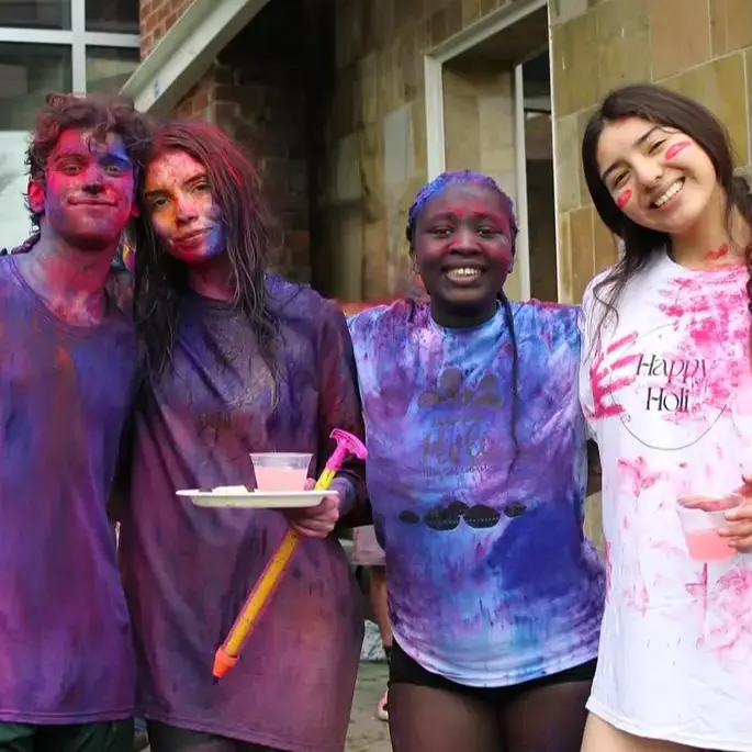 Four Skidmore students covered in colorful powder smile together after participating in the Holi festival