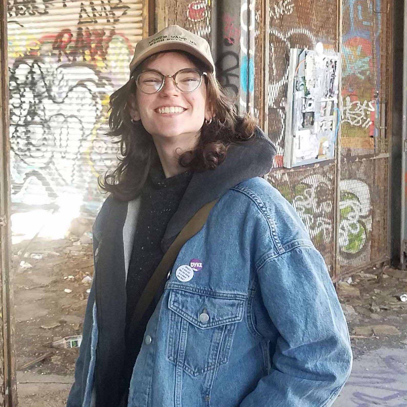 Tori smiles in a jean jacket before a graffiti wall