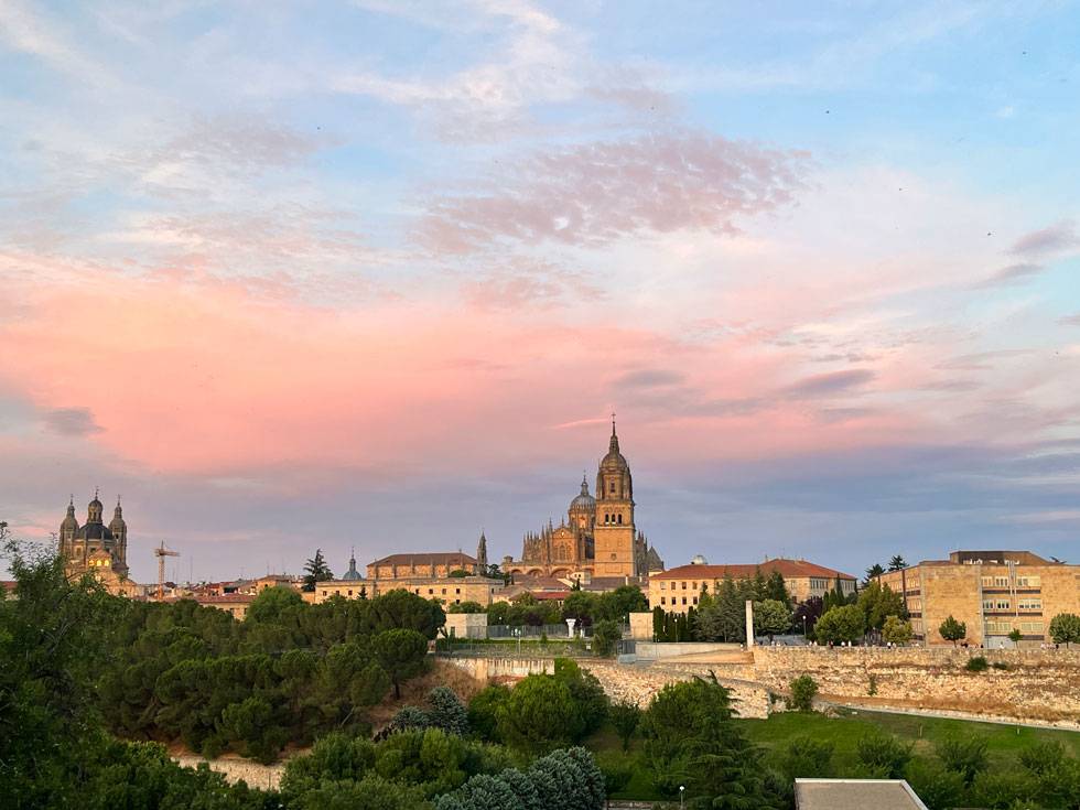 Spanish cathedral constructed out of white stone and a red roof with a blue and pink sky background. 
