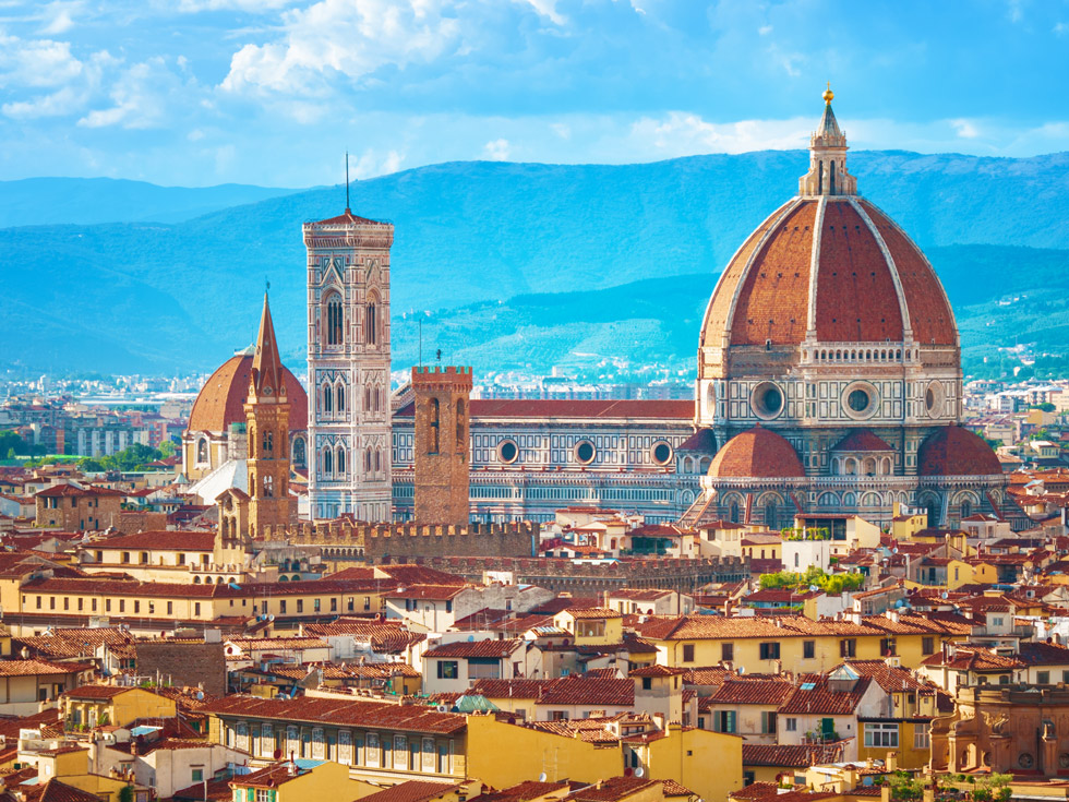 A bird eyes view looking out over Florence, Italy with the Cathedral of Santa Maria del Fiore rising up in the background and the yellow and red smaller building in front.