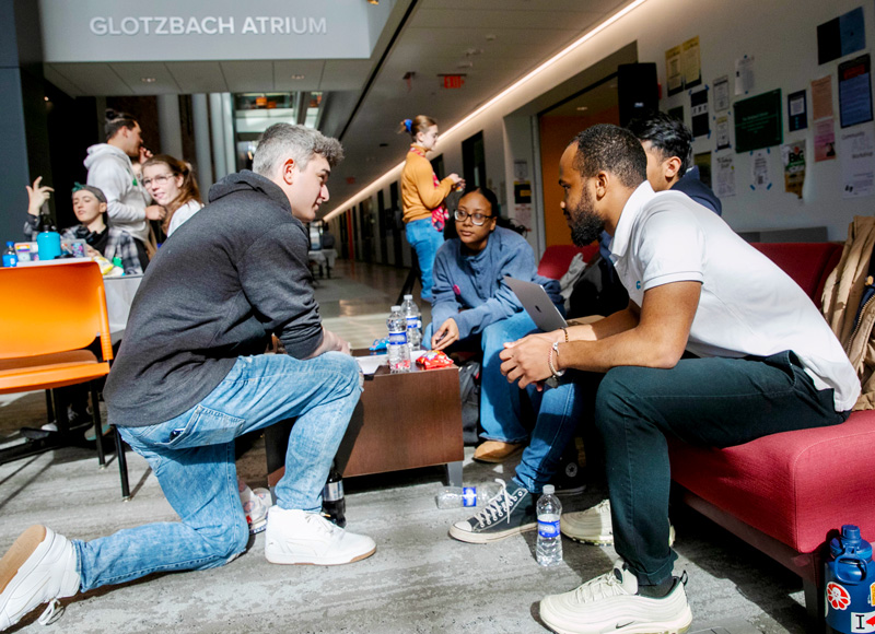 four college students gather around a couch to brainstorm